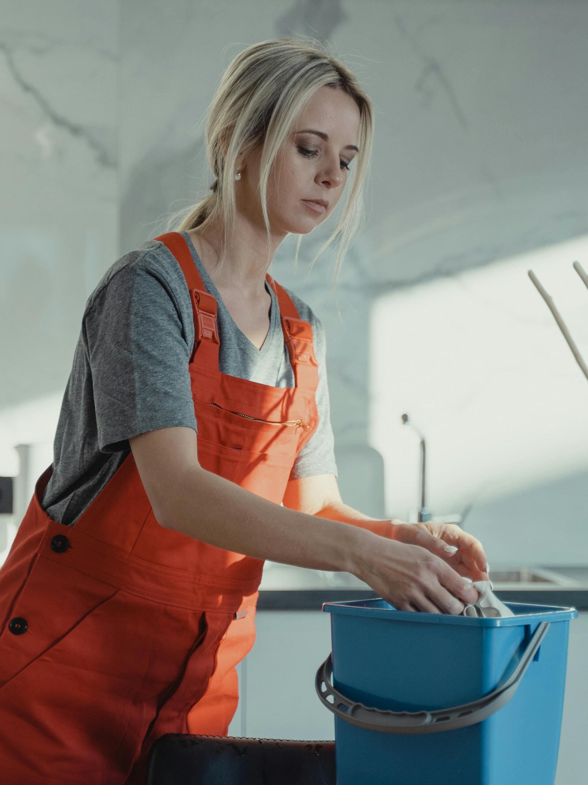 Reinigungskraft legt Tuch in Eimer in Küche während Wohnungsreinigung